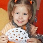 Little girl holding up paper snowflake and smiling