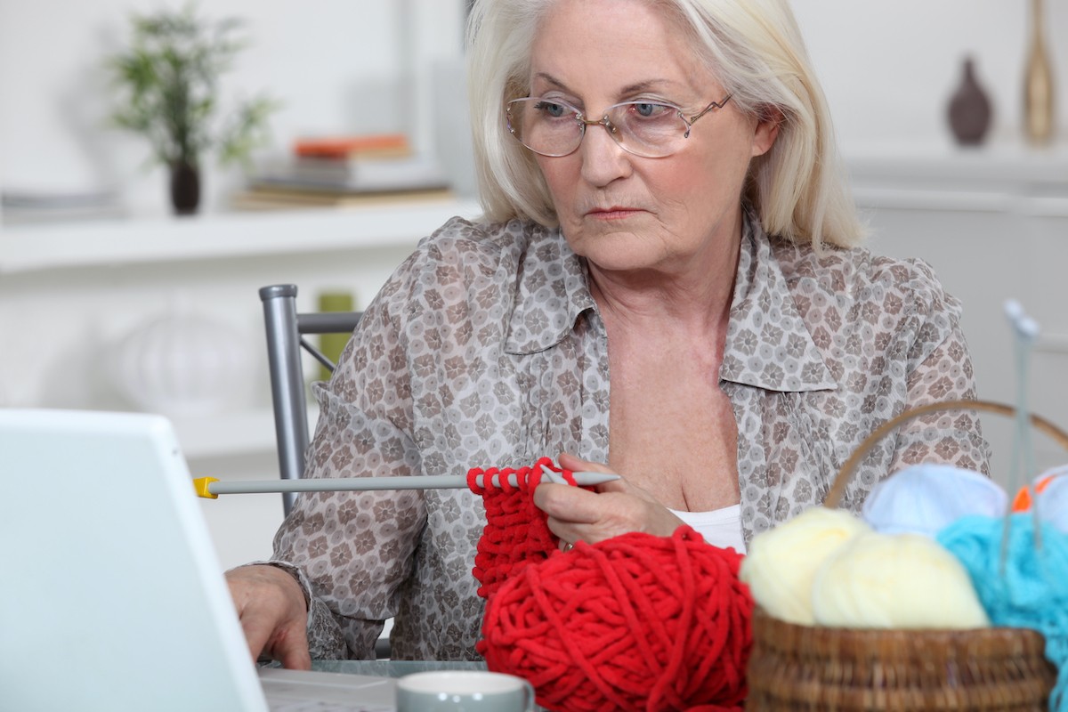 Mature woman knitting at computer looking not so happy